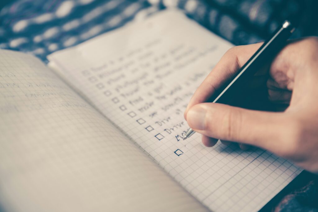 Close-up of a person's hand writing in a notebook with a checklist, featuring neatly written items on graph paper.