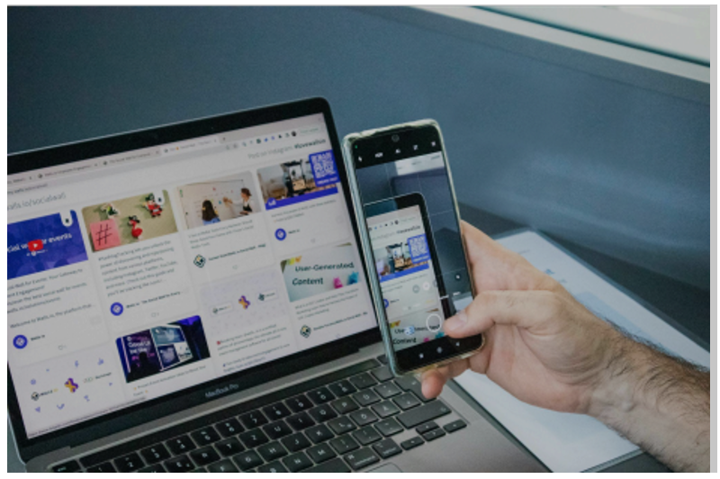 Hands holding a smartphone while a laptop screen shows a social platform dashboard, symbolizing multitasking between engagement and strategy.