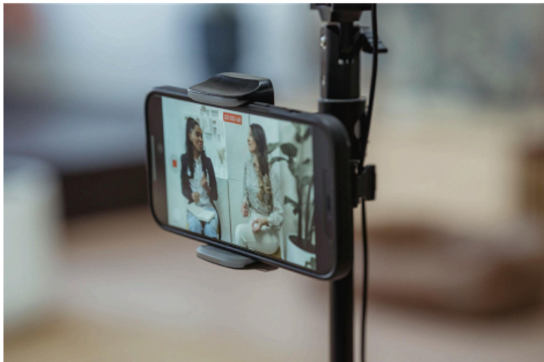 Individual speaking directly into a smartphone camera mounted on a tripod, with business context in the background great for DIY video content or Facebook Live.