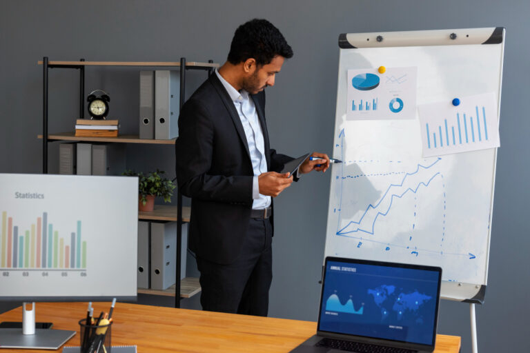 Business professional in a suit presenting data analysis on a whiteboard with charts, graphs, and statistics, while holding a tablet in a modern office setting.