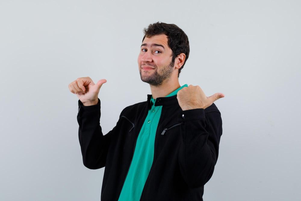 Confident man pointing both thumbs toward himself with a proud expression against a plain background.