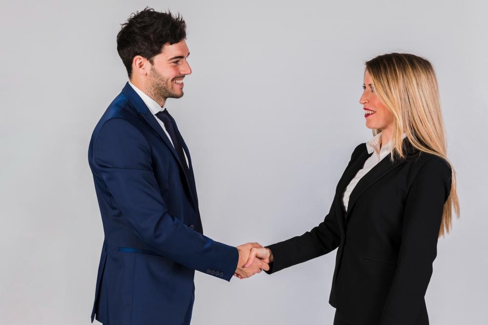 A man and a woman in formal business attire shaking hands and smiling at each other.