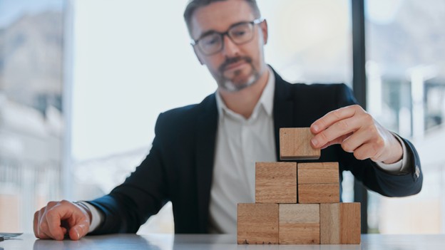 A man in a suit carefully stacks wooden blocks, symbolizing strategic building in business and marketing.